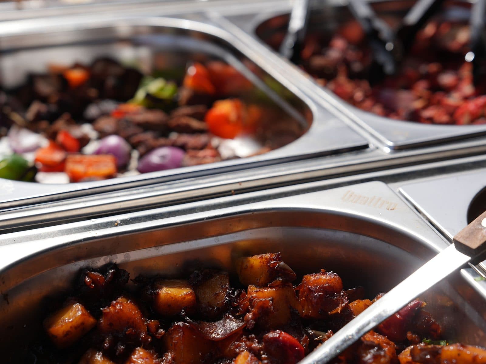 Two chafing trays on the counter: grilled meat with peppers and red onion above, a dark potato masala below.
