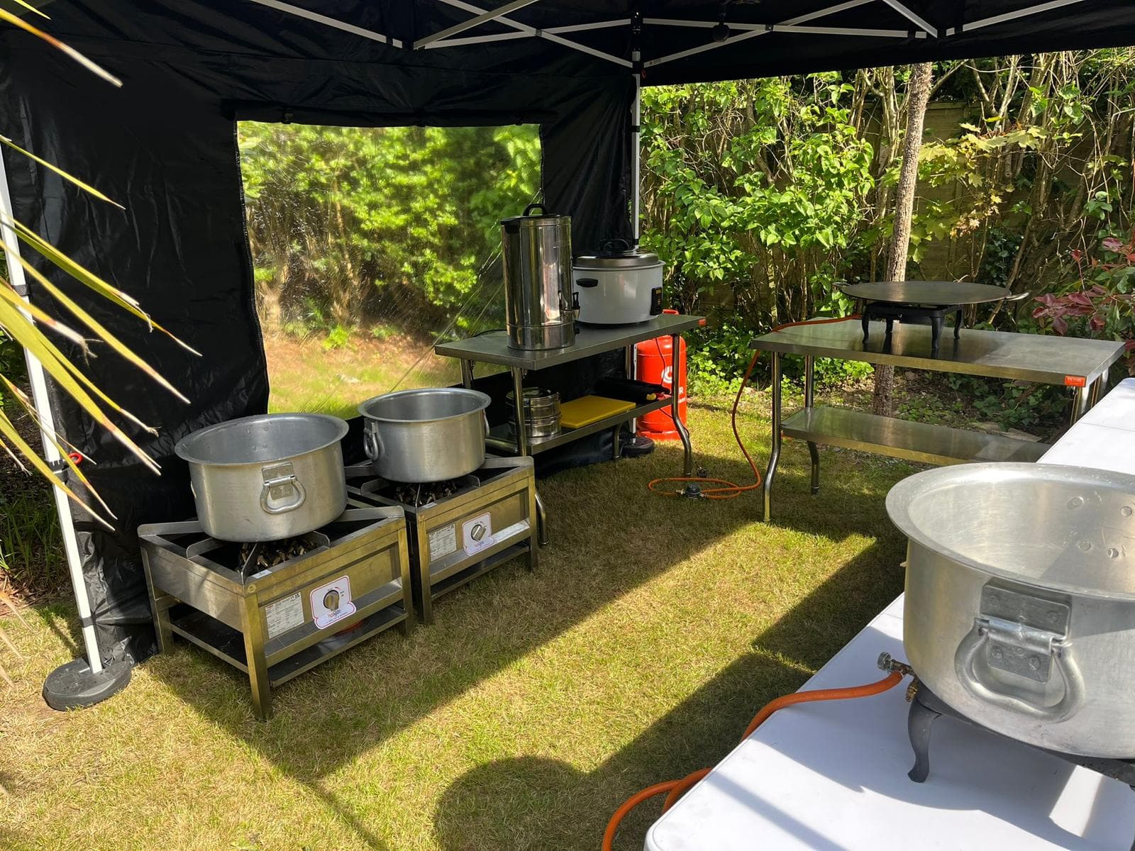 Inside the gazebo: two large karoga pots on LPG burner stands, with a tea urn, rice cooker and gas bottle set up on stainless steel tables.